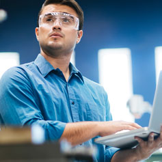 man with safety glasses holding laptop open in hand