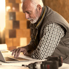 older man leaning over using trackpad on laptop